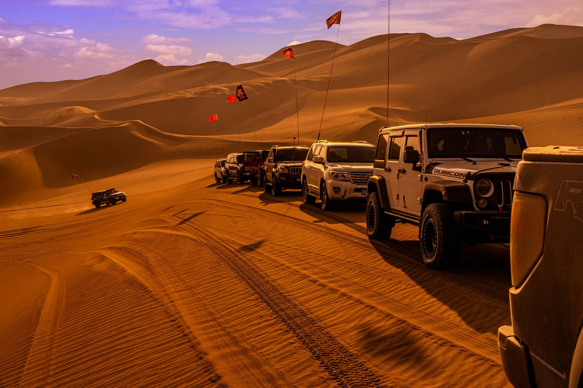 A line of off-road vehicles crossing golden sand dunes