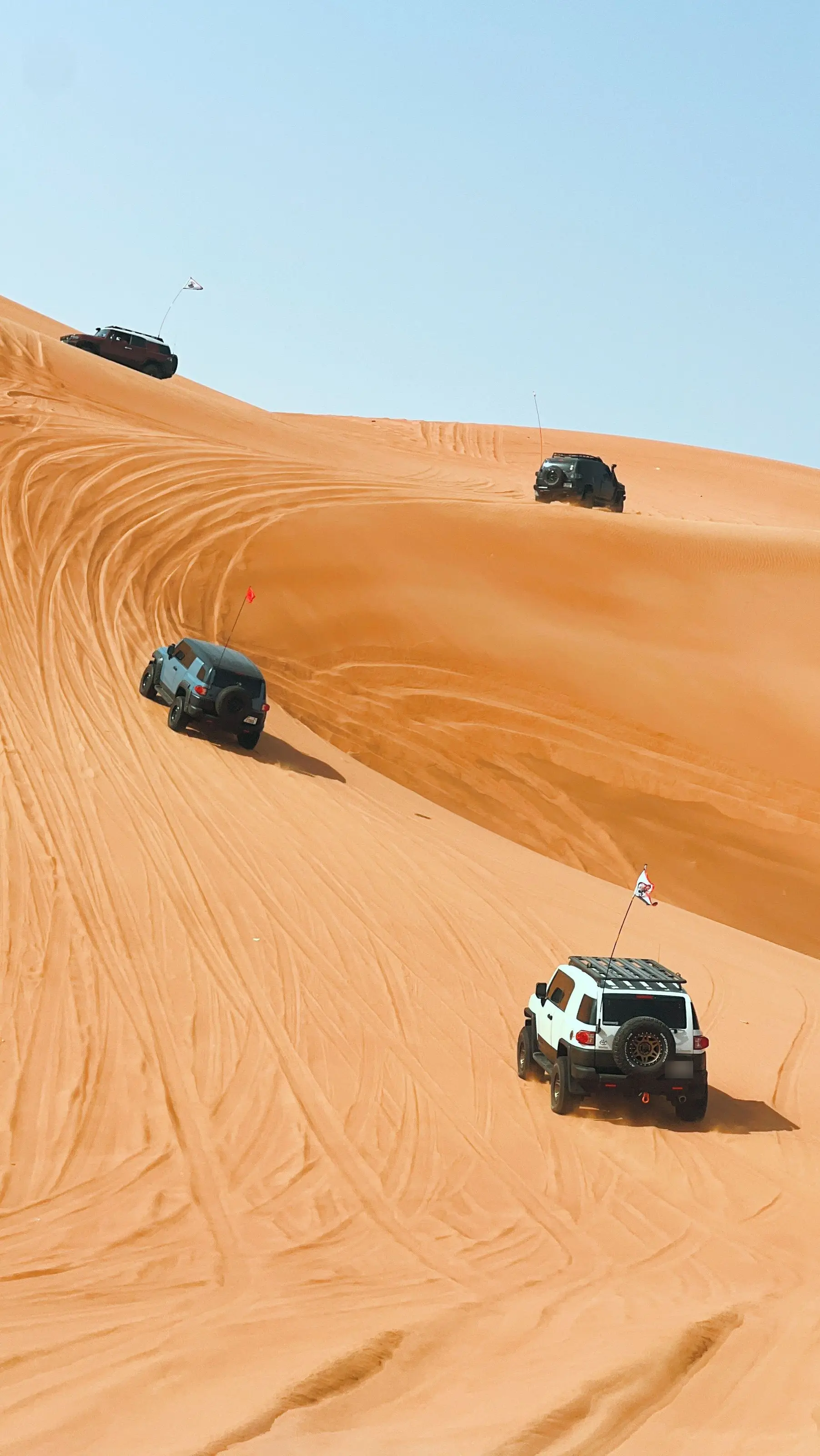 Four off-road vehicles climbing a sand dune under a blue sky