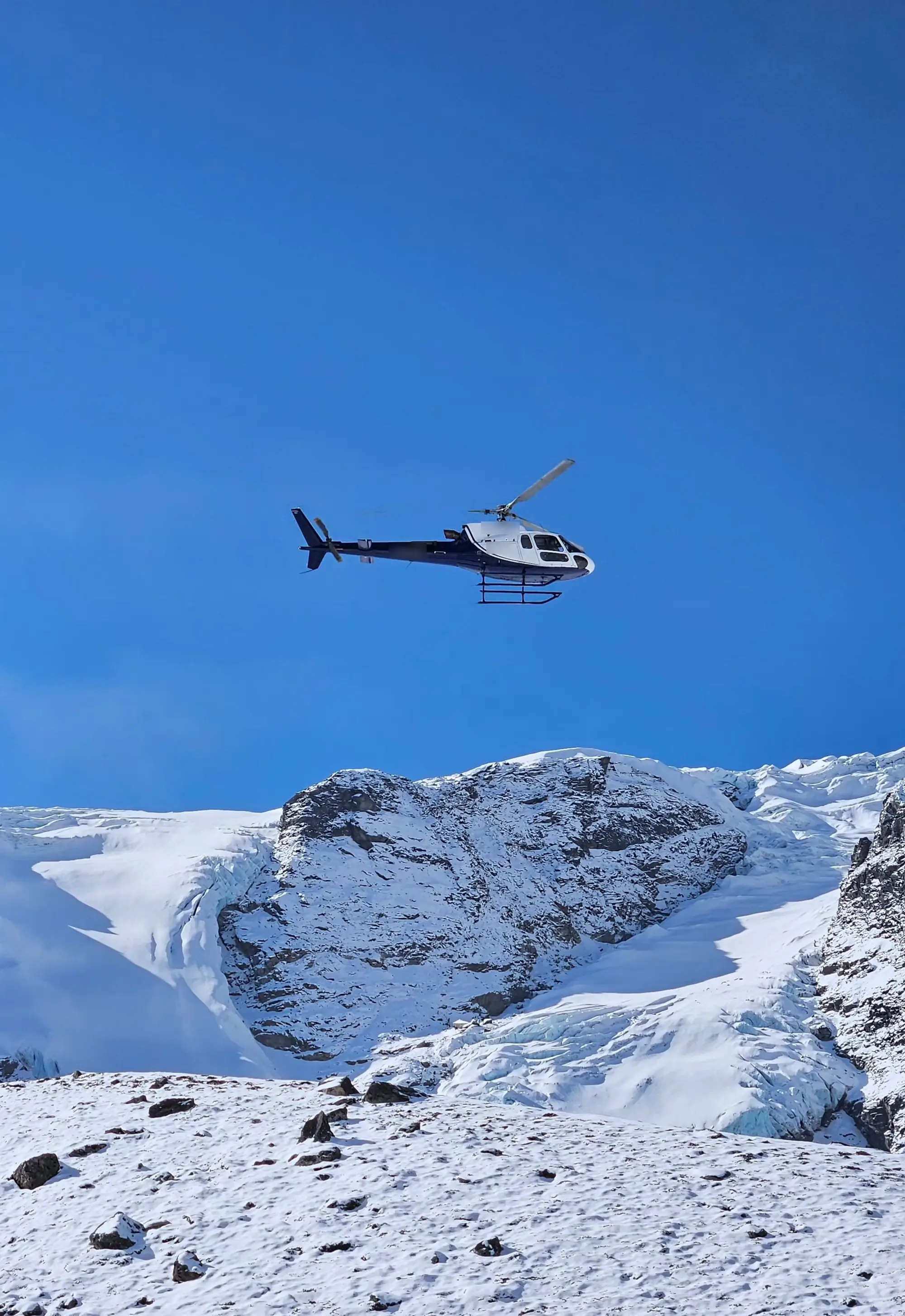 A tour helicopter flying over snowy mountain peaks under a deep blue sky