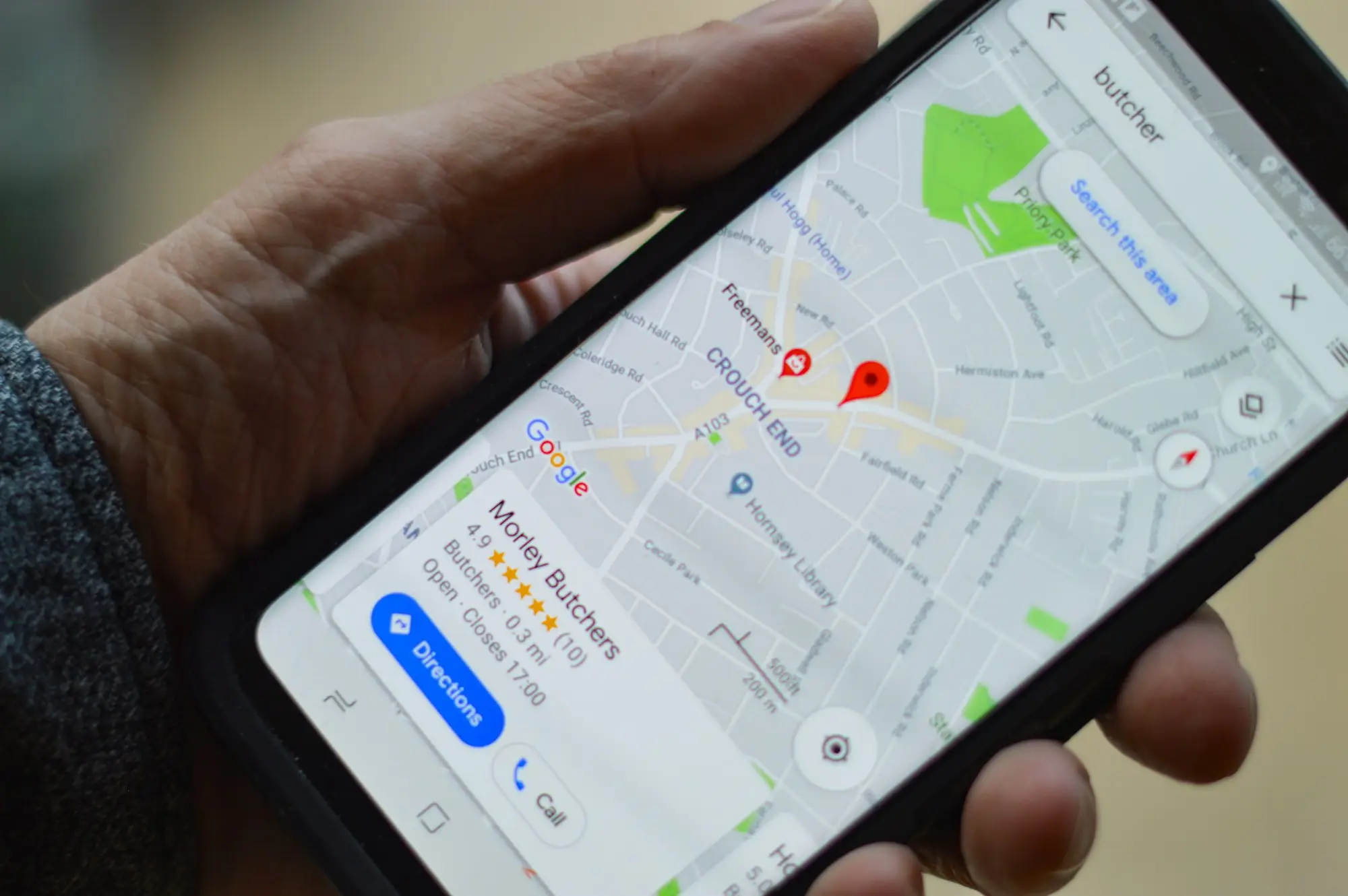 A hand holding a phone showing a Google Maps listing