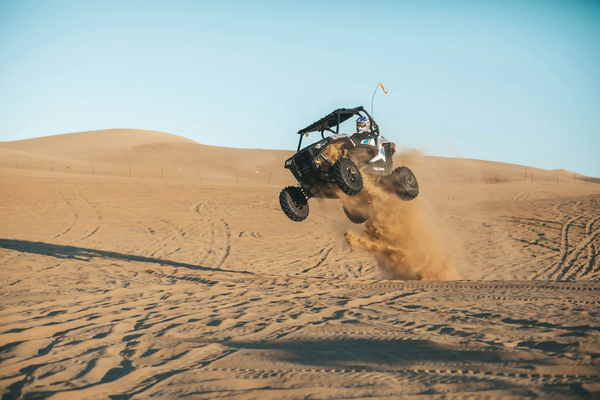 A side-by-side off-road vehicle catching air on a sand dune