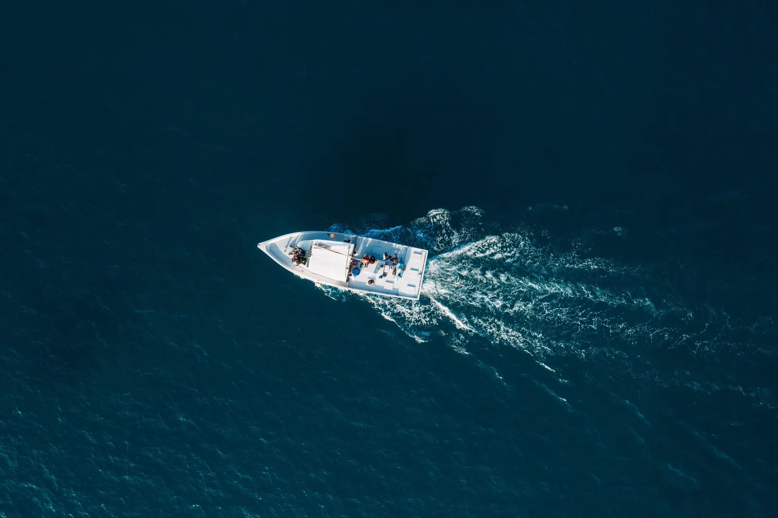 A boat with guests under way on deep blue water, seen from above